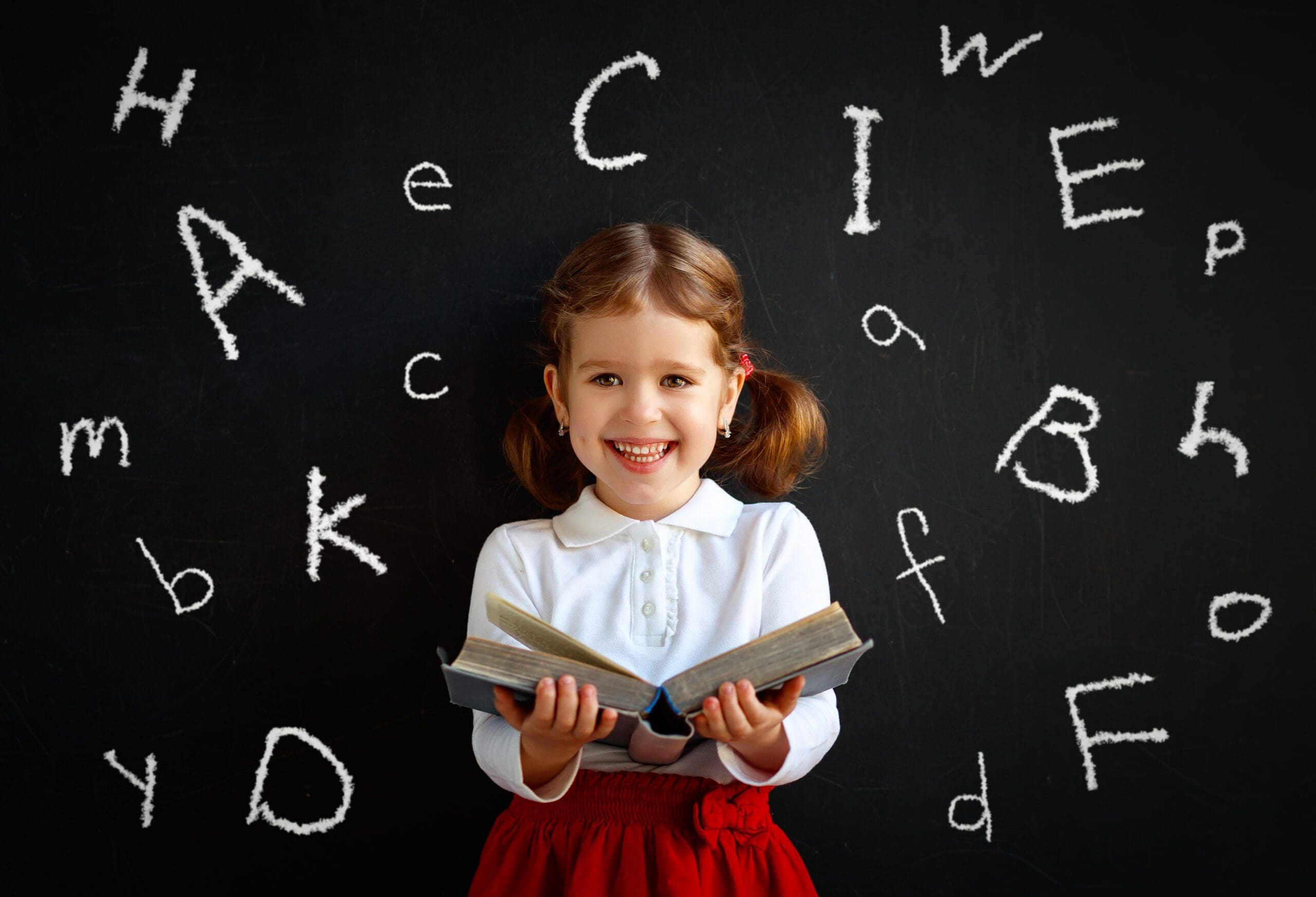 Little girl holding a book with the letters of the alphabet behind her